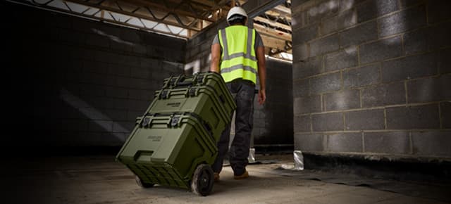 Tradesman wheeling stacked BUNKER Load-Up tool boxes through a building site