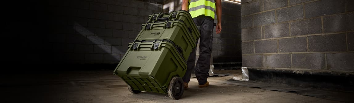 Tradesman wheeling stacked BUNKER Load-Up tool boxes through a building site